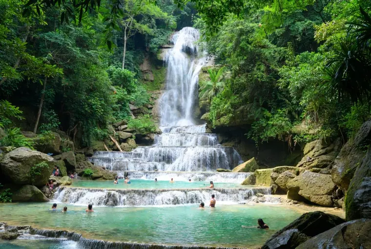 Multi-tiered Erawan Waterfall with turquoise pools and people swimming in Kanchanaburi