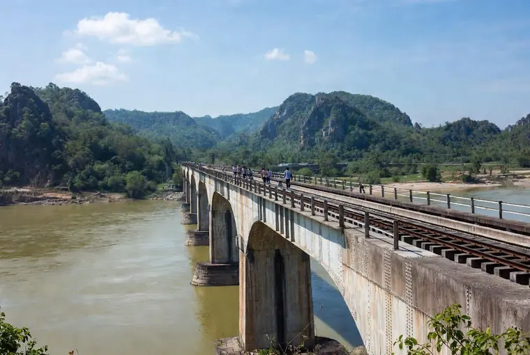 The Bridge over the River Kwai in Kanchanaburi with people walking across and green hills behind