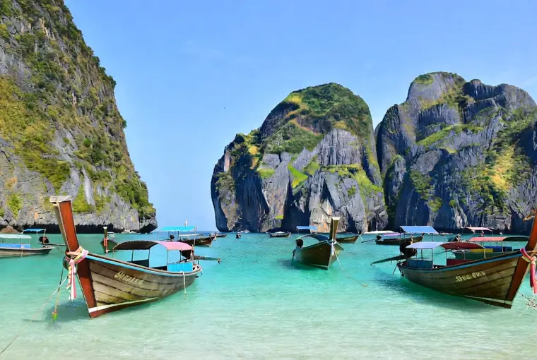 Longtail boats in turquoise water surrounded by limestone cliffs on Koh Phi Phi