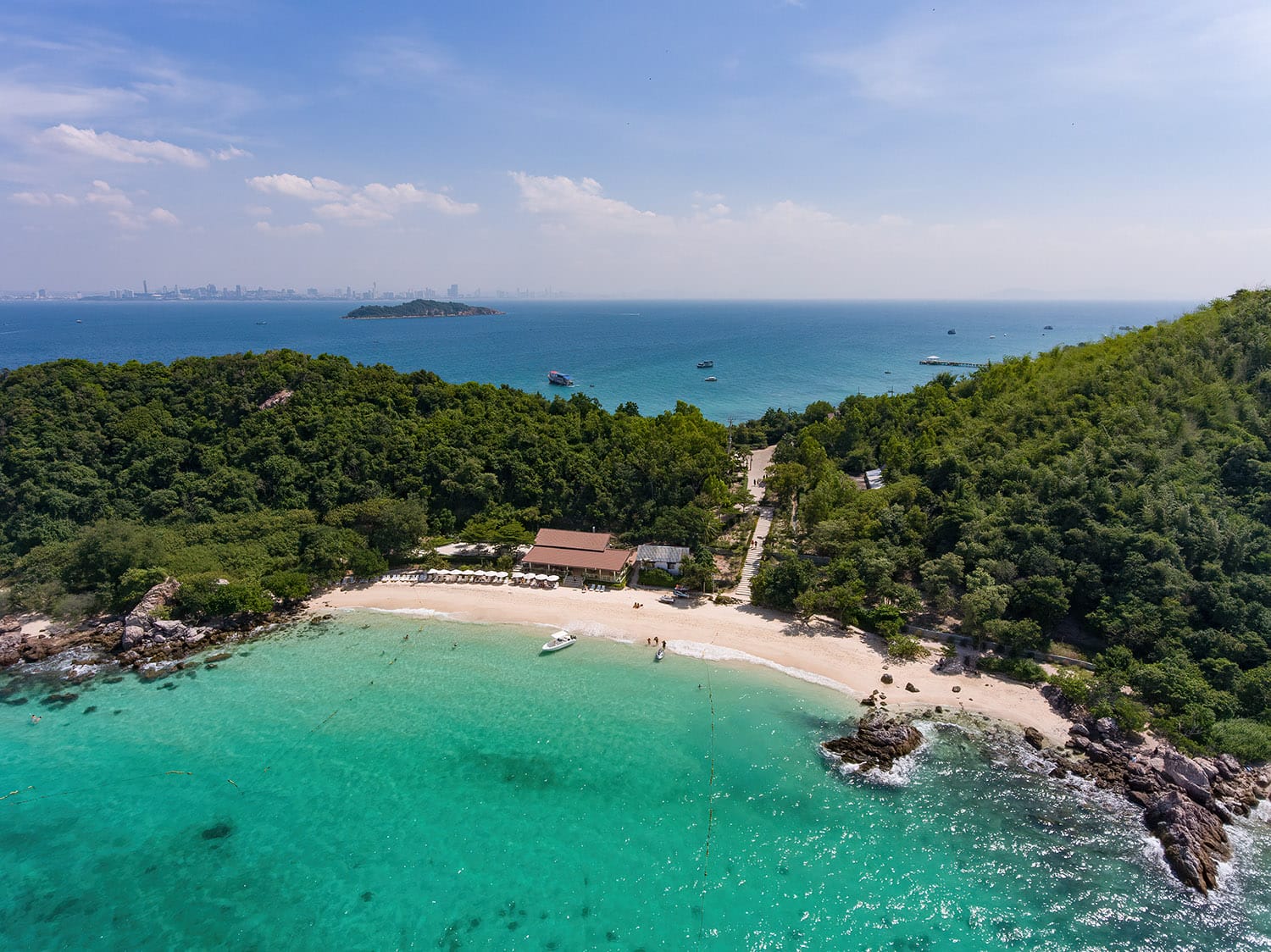 Aerial view of a turquoise cove and white-sand Koh Larn beach near Pattaya, with the Pattaya skyline on the horizon