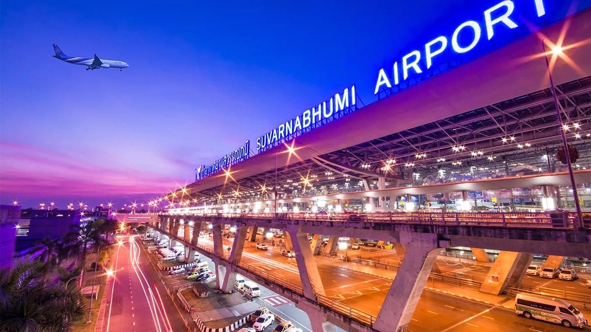 Suvarnabhumi Airport departures viaduct in Bangkok lit up at dusk with an aircraft overhead, the focus of this Thailand travel news update on baggage screening