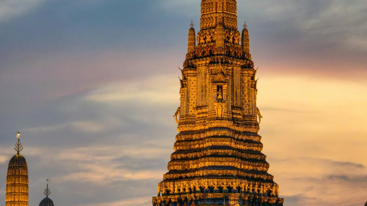 Wat Arun, the Temple of Dawn, glowing gold at dusk beside the Chao Phraya River in Bangkok, the destination of the 2026 Royal Barge Procession and a highlight of Bangkok tourism