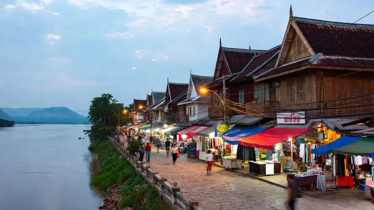 Riverside wooden shophouses and a busy evening walking street market in northern Thailand at dusk, the kind of community festival setting that fills the Thai festivals 2026 September calendar