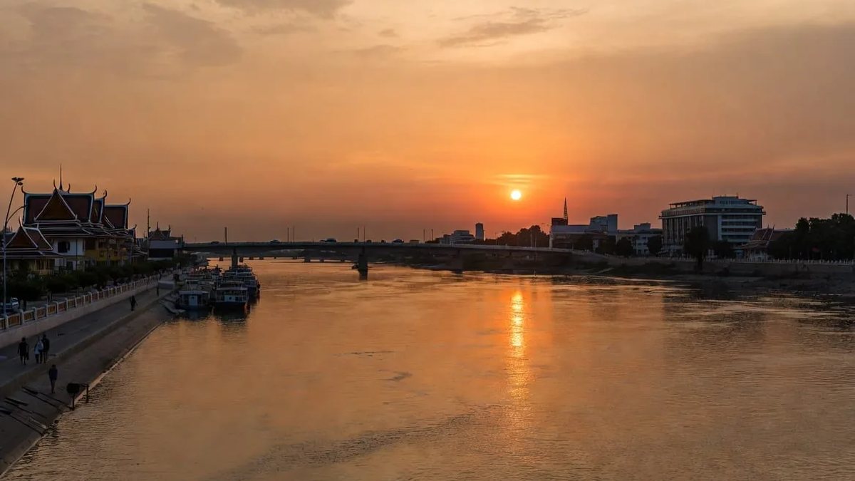 Sunset over the Mekong River at Nong Khai with the riverside promenade, moored boats and the Thai-Lao Friendship Bridge in the distance, one of the best places to visit in Thailand in October
