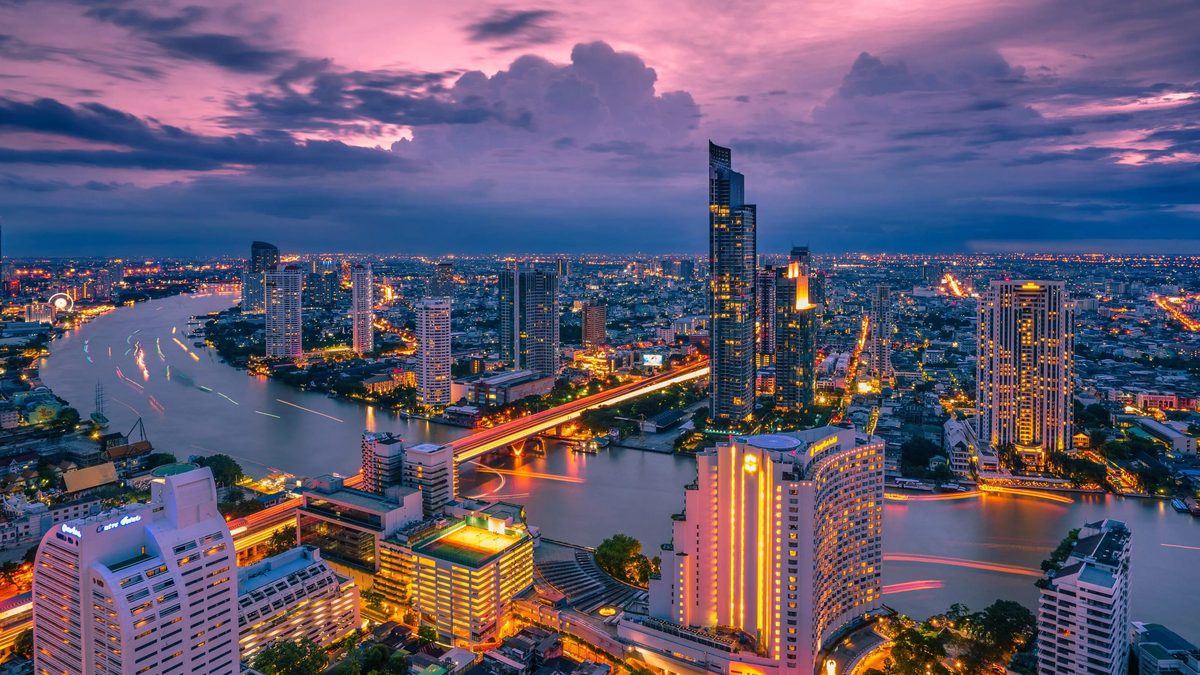 The Chao Phraya river curving through Bangkok at dusk with riverboats and lit towers, the starting point for the Amphawa day trip in this Thai festivals 2026 guide