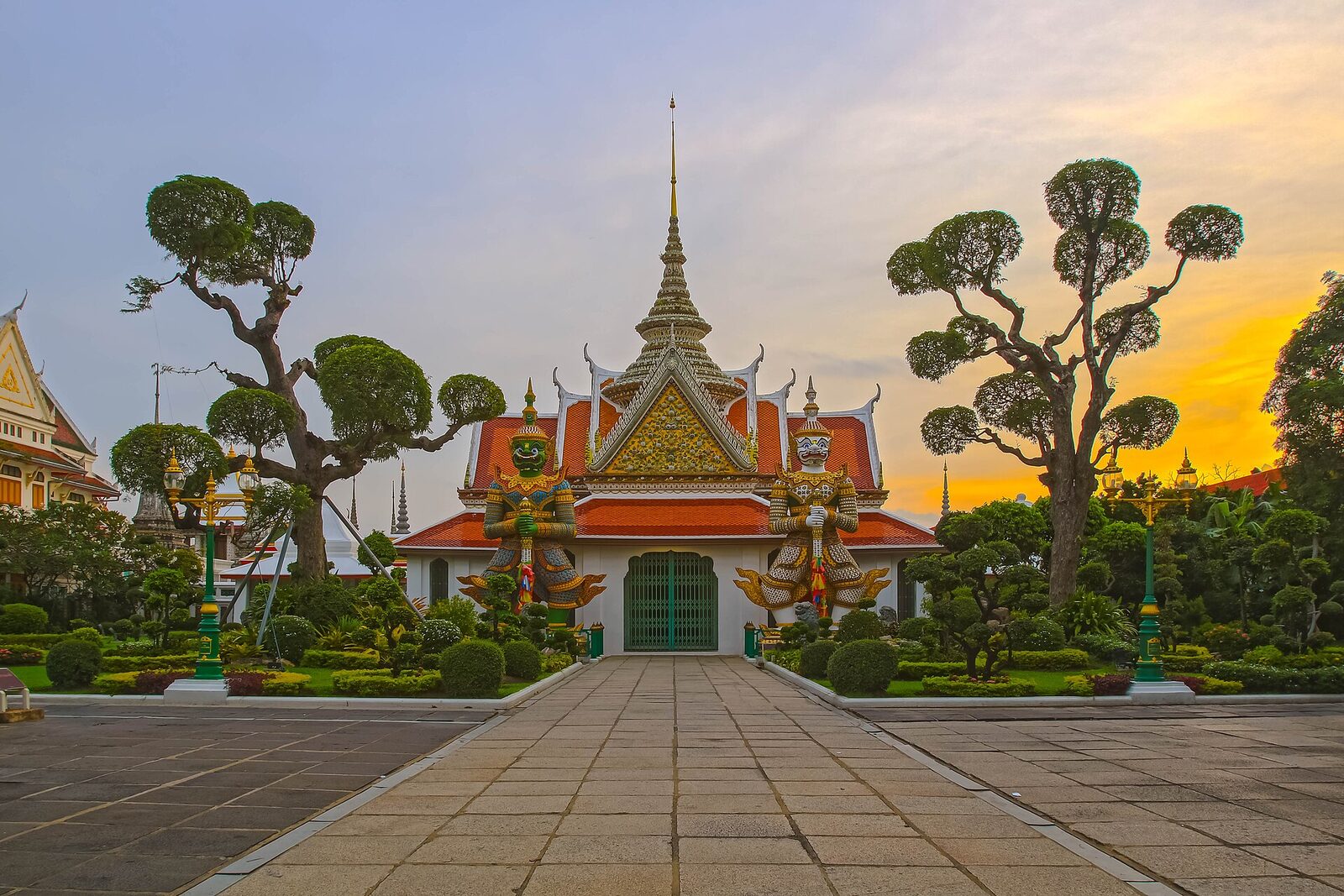 Wat Arun in Bangkok at sunset with giant guardian statues flanking the ordination hall gate, a headline stop for visitors following Thailand travel news