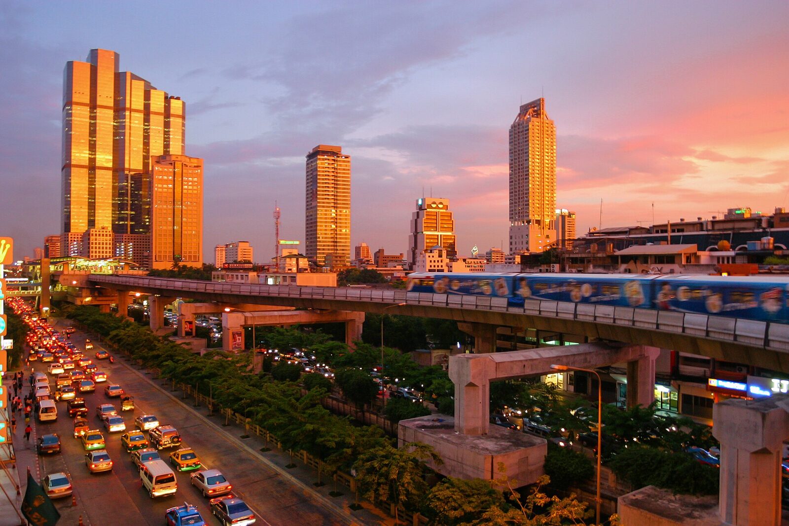 A BTS Skytrain train crossing an elevated viaduct above heavy Bangkok traffic at sunset, the elevated rail network that kept running through the 2026 Bangkok floods