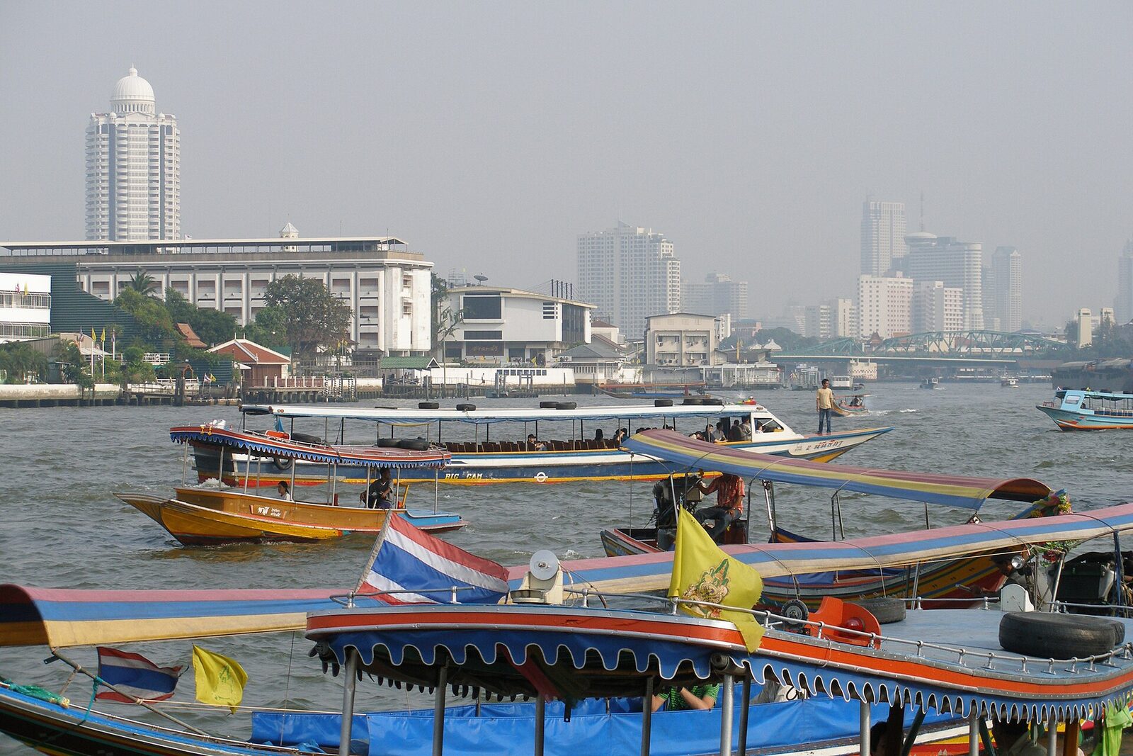 Express boats and longtail boats on the Chao Phraya River in Bangkok with the city skyline behind, river transport that remains a reliable way to reach riverside temples in this Bangkok tourism update