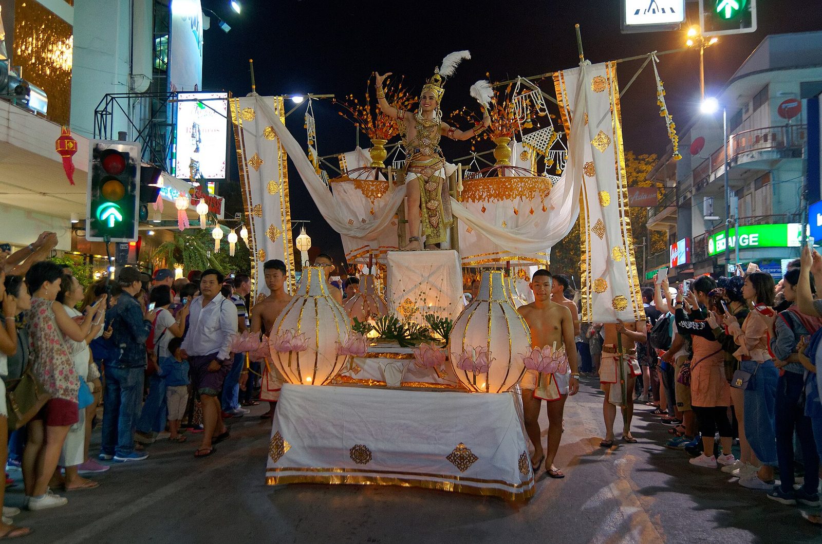 A gold and white Loy Krathong parade float carrying a costumed dancer moves down a Chiang Mai street lined with spectators at night, the centrepiece procession of Thai festivals 2026