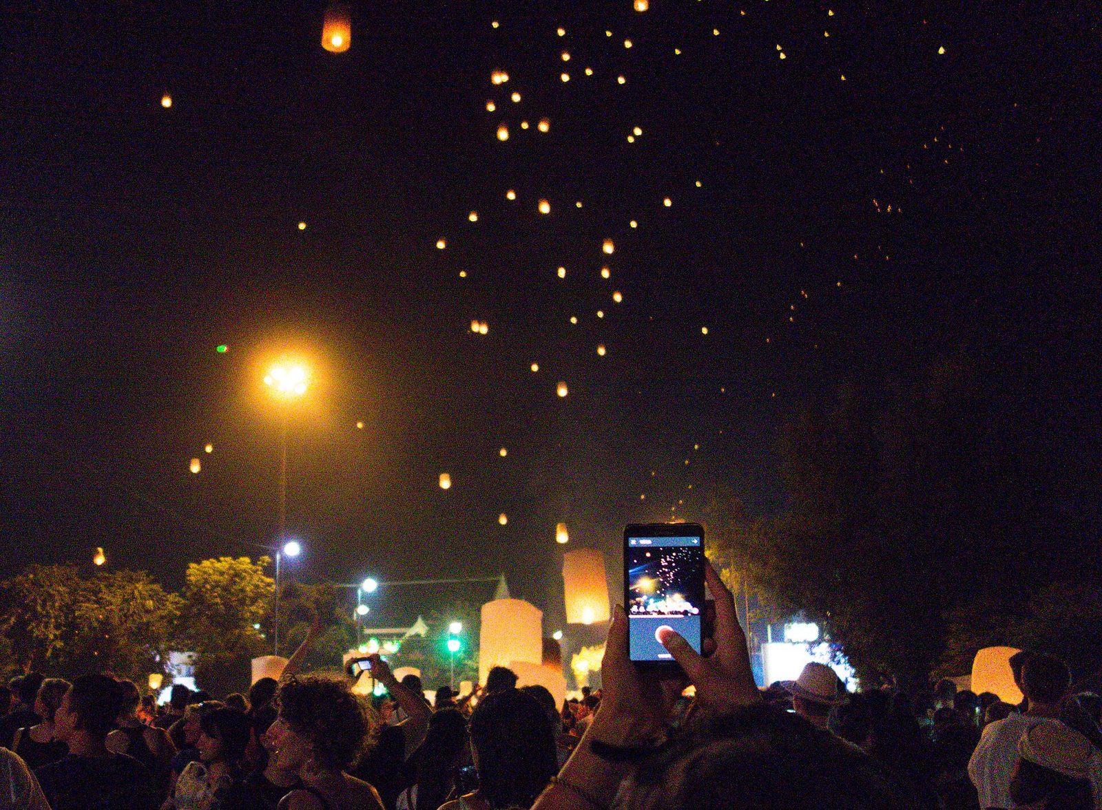 Hundreds of glowing khom loi sky lanterns drifting into the night sky above a crowd in Chiang Mai during Yi Peng, the most photographed of the Thai festivals 2026