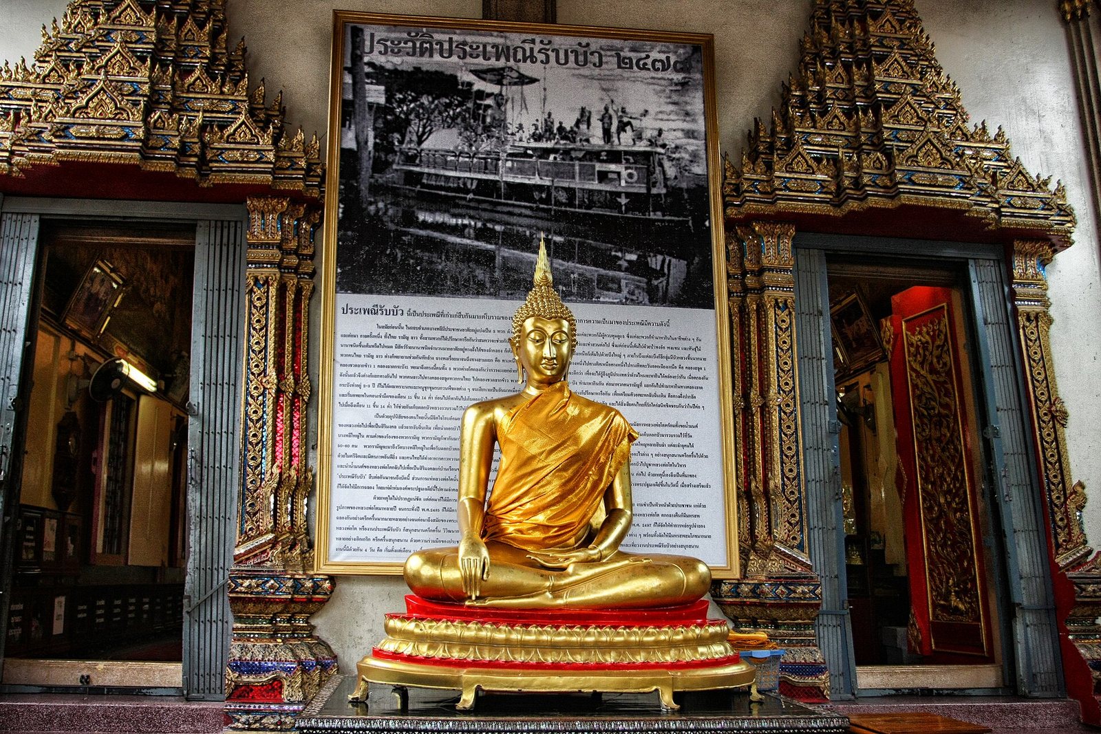 Gilded Buddha image at Wat Bang Phli Yai Nai in Samut Prakan seated in front of a large board telling the history of the Rap Bua lotus festival, an easy day trip for Bangkok tourism