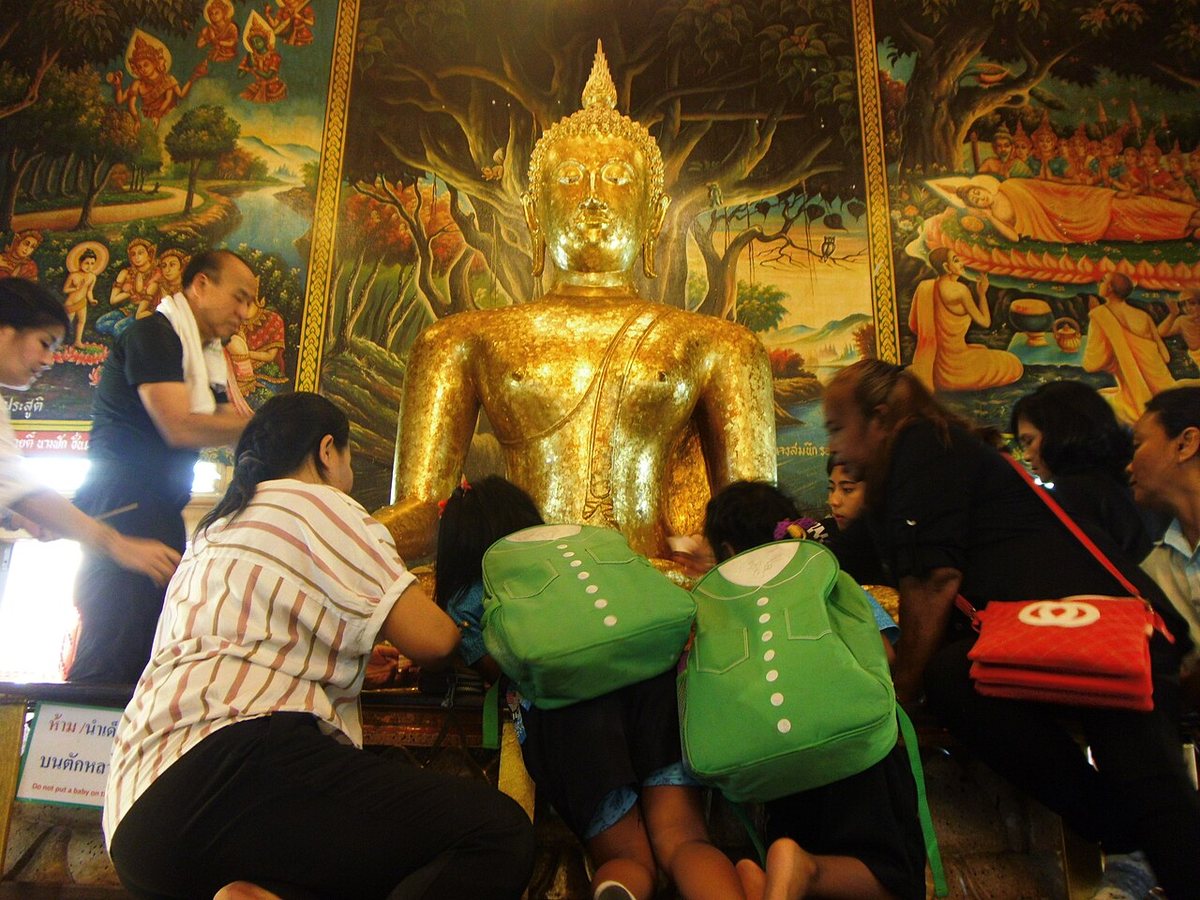 Worshippers kneeling to press gold leaf onto the Luang Pho To Buddha image inside Wat Bang Phli Yai Nai, Samut Prakan, the image at the centre of the Rap Bua lotus festival and a highlight of Thai culture near Bangkok