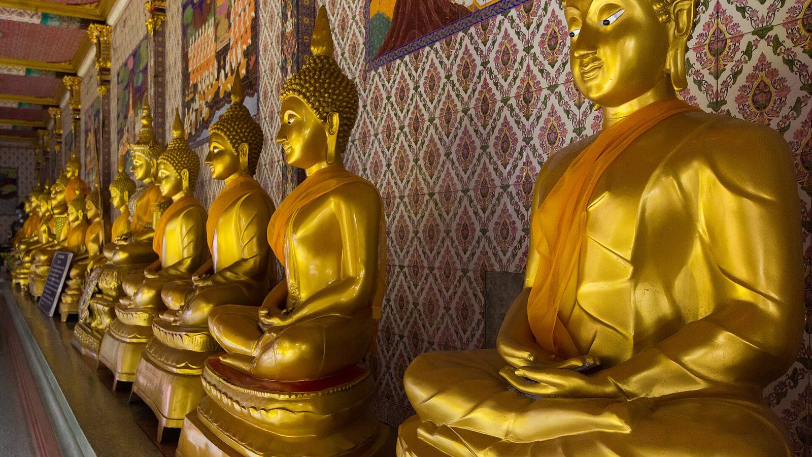 Row of gilded seated Buddha images along the cloister wall at Wat Bang Phli Yai Nai in Samut Prakan, a quiet temple visit within easy reach of Bangkok tourism itineraries