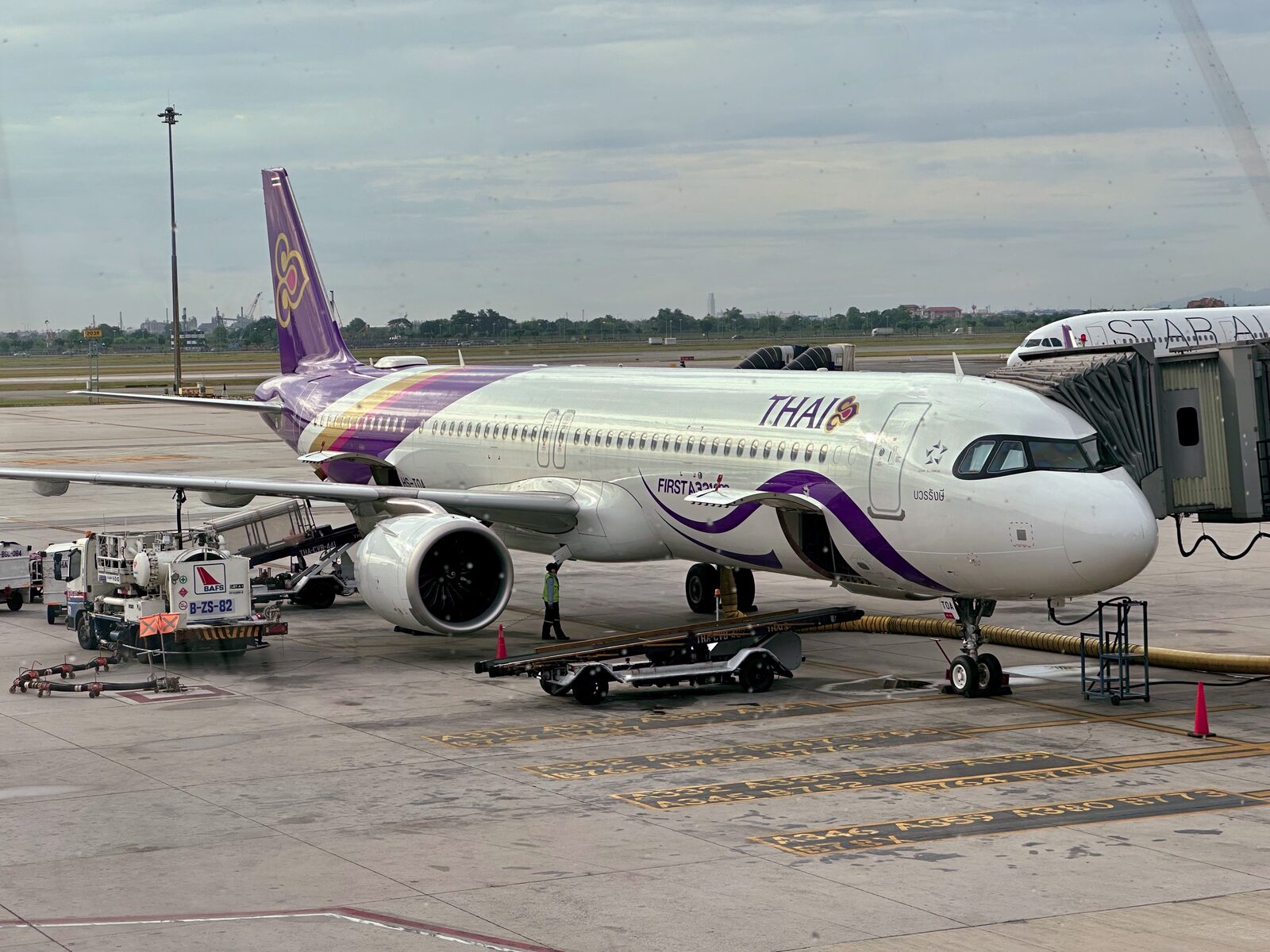 Thai Airways Airbus A321neo parked at a Suvarnabhumi Airport gate in Bangkok with ground handling crew and a fuel truck alongside, the subject of this Thailand travel news update on flight delays and compensation