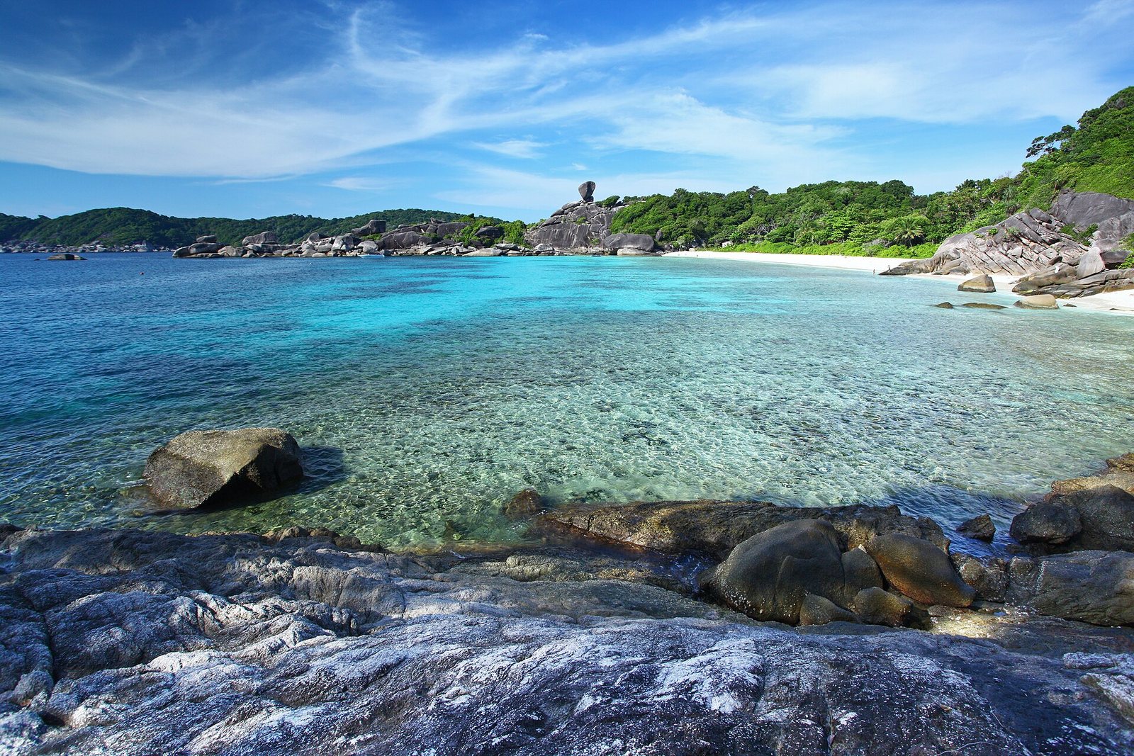 Clear shallow turquoise water over granite boulders and white sand at Donald Duck Bay on Koh Similan, with Sail Rock on the headland, among the best places to visit in Thailand for snorkelling