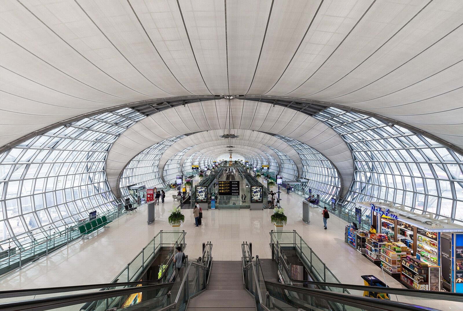 The vaulted glass-and-steel concourse of Suvarnabhumi Airport in Bangkok with passengers walking between gates, the hub at the centre of this Thailand tourism update on free transit stopover tours