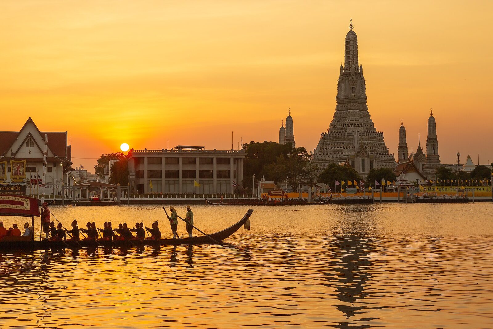 A royal barge rowed past the white prang of Wat Arun at sunset on the Chao Phraya River in Bangkok, the destination of the 6 November 2026 Royal Barge Procession