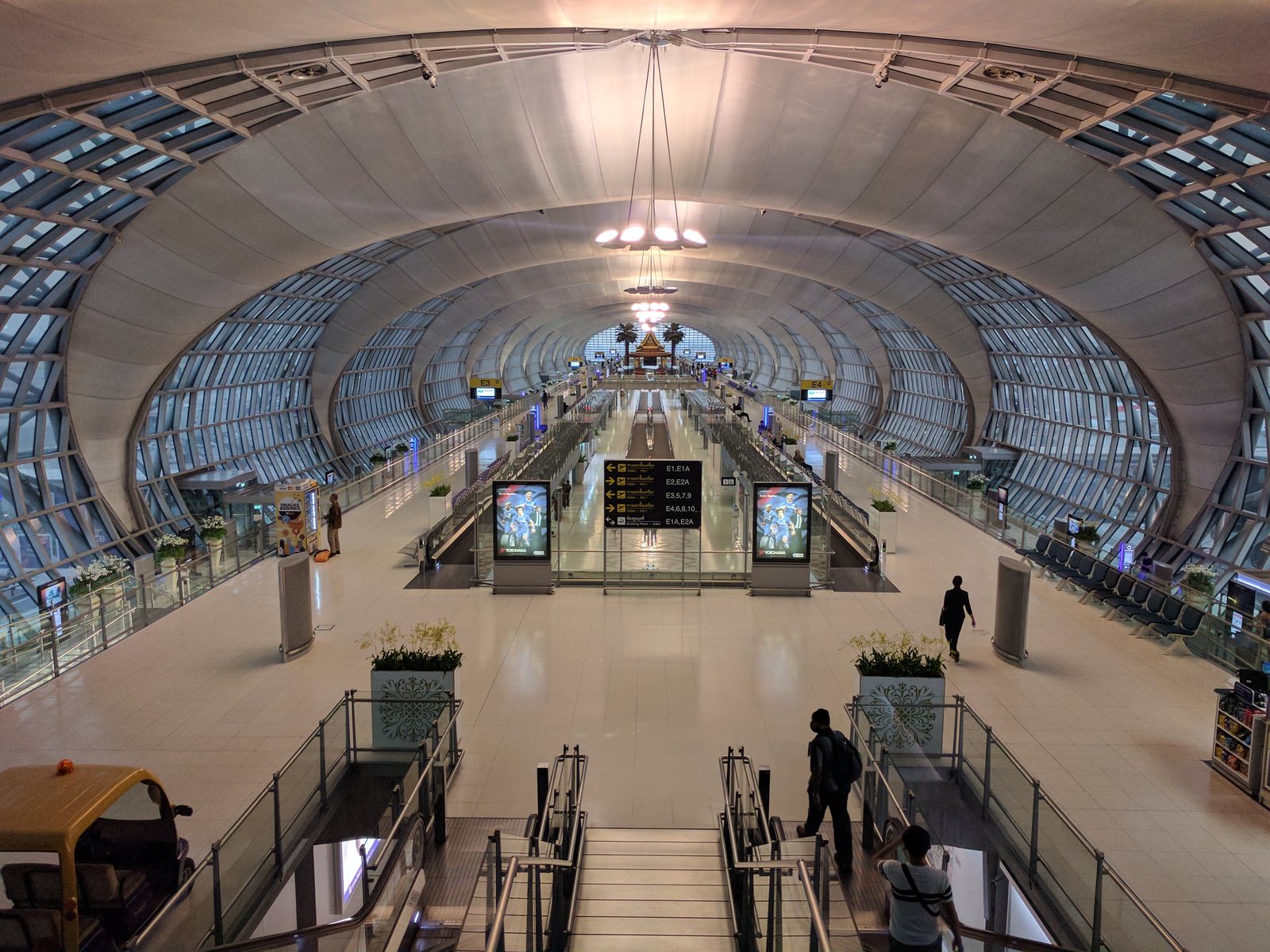 The vaulted glass and steel concourse of Suvarnabhumi Airport in Bangkok with travellers on the escalators, arrival point for the new daily Kuala Lumpur to Bangkok flights