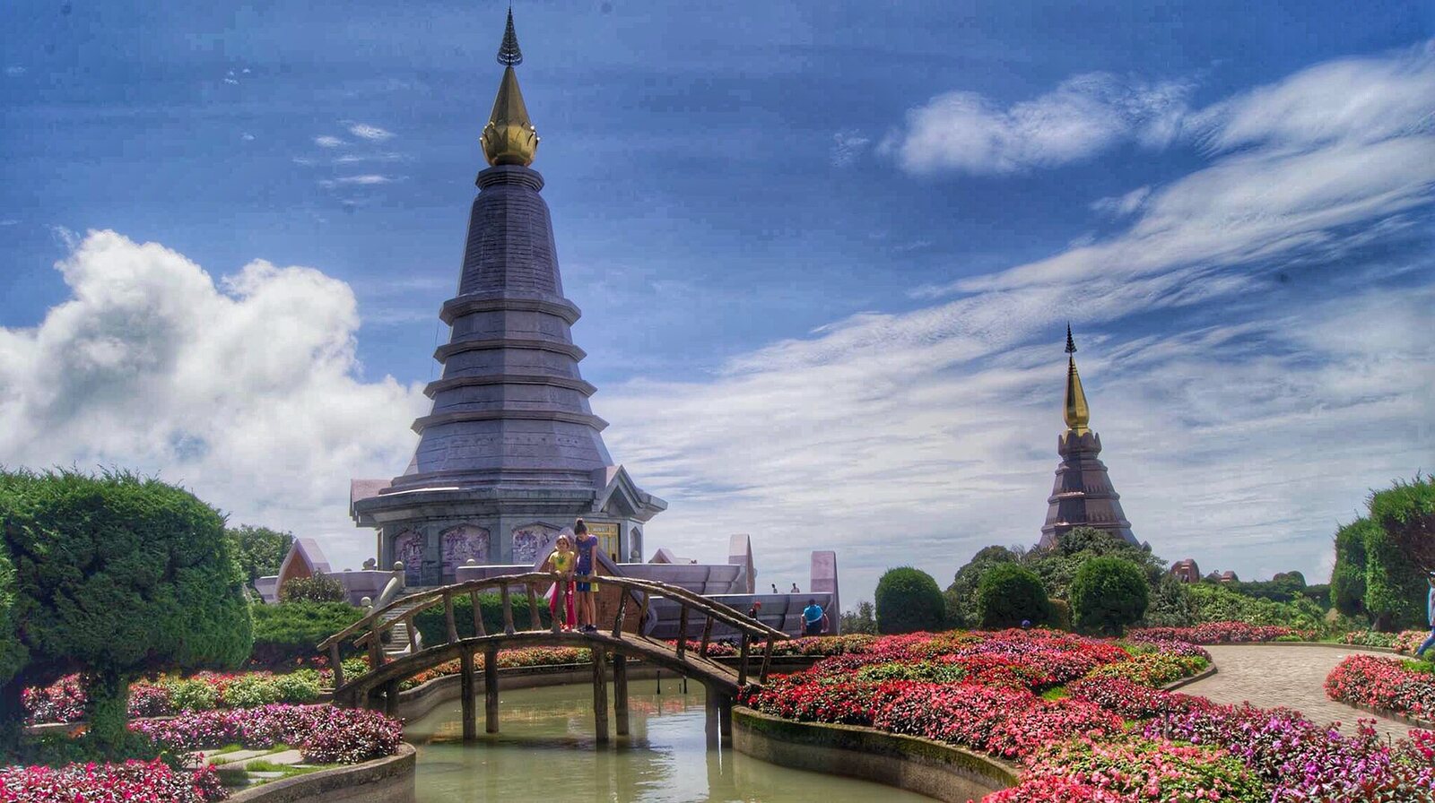 The twin royal pagodas on Doi Inthanon under a bright blue sky with flower beds and an arched wooden bridge in the foreground, northern Thailand at the start of the cool season