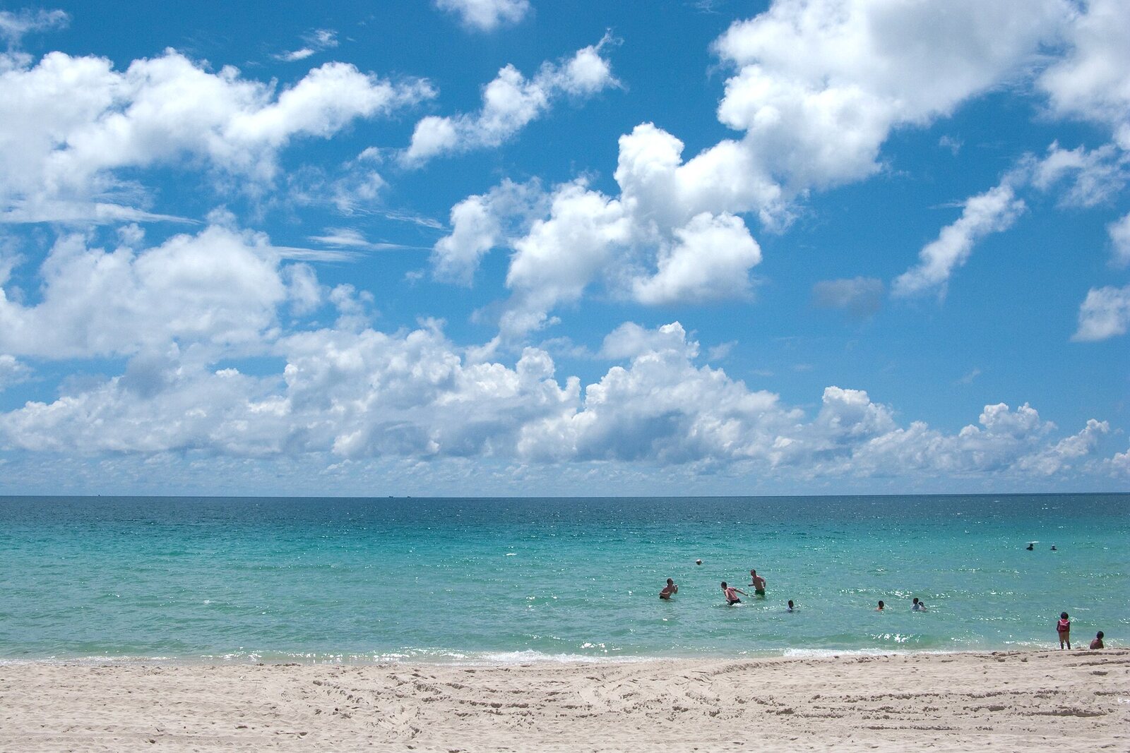 A wide empty white sand beach and turquoise sea under blue sky with cumulus cloud on Koh Samui, a Gulf of Thailand island whose wet season runs opposite to the rest of the country