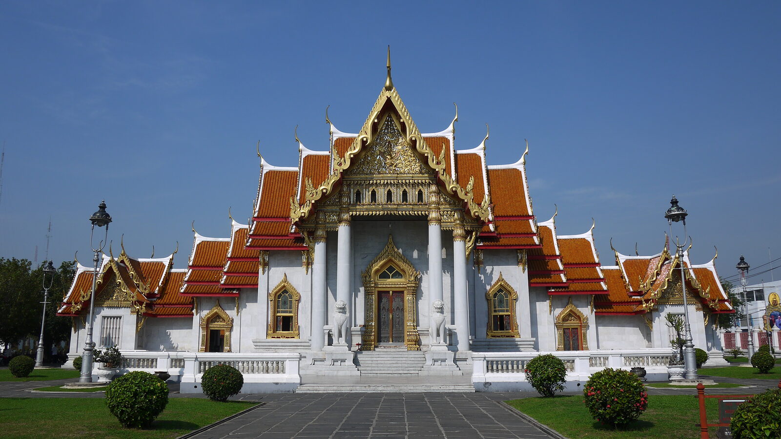 The white Carrara marble ordination hall of Wat Benchamabophit in Dusit, Bangkok, with orange tiled roofs and gilded gables under a blue sky, a key Bangkok tourism stop on Chulalongkorn Memorial Day
