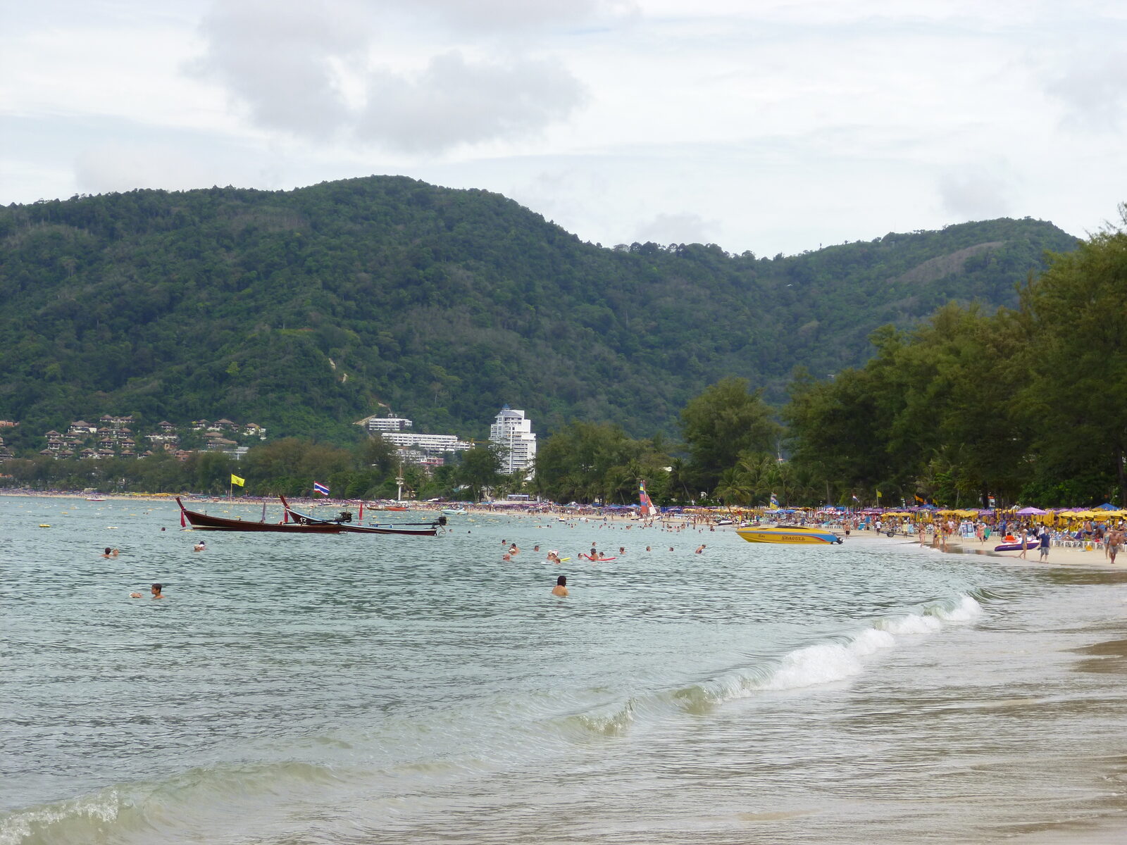 The broad curve of Patong Beach in Phuket with longtail boats, sun loungers and forested hills behind, one of the best places to visit in Thailand on the Andaman coast
