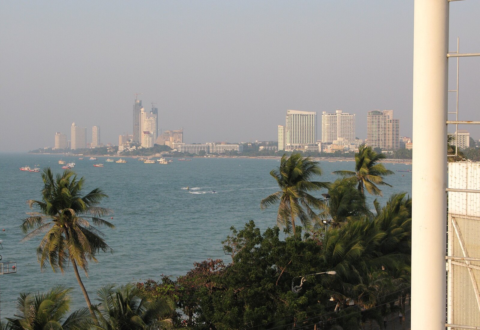 Pattaya Bay from the beach on a clear cool-season morning, curving sand and high-rises behind, the daytime side of Thailand vacation planning in Pattaya