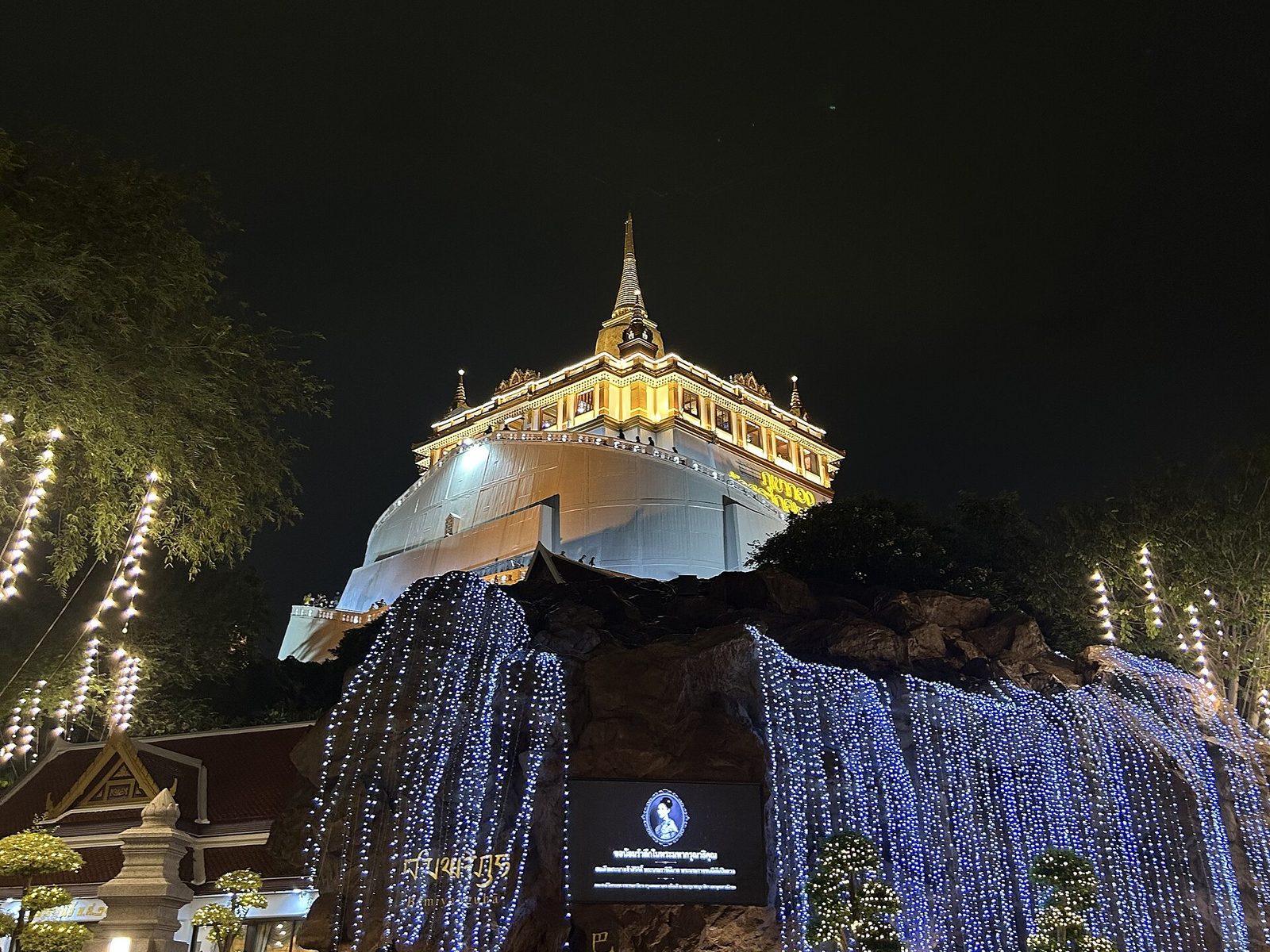 The Golden Mount at Wat Saket lit up at night during the Golden Mount Temple Fair in Bangkok, Thailand, with curtains of fairy lights over the rock base