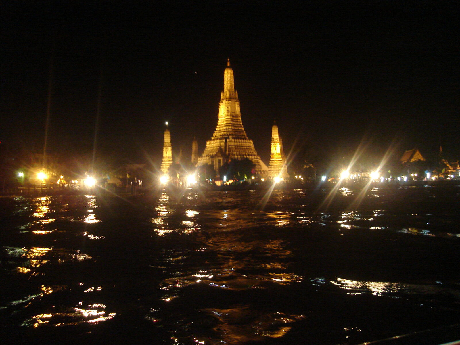 Wat Arun's porcelain-studded prang lit gold at night above the dark Chao Phraya River in Bangkok, a Thai culture landmark and one of the illuminated sites in the Vijit Chao Phraya light festival