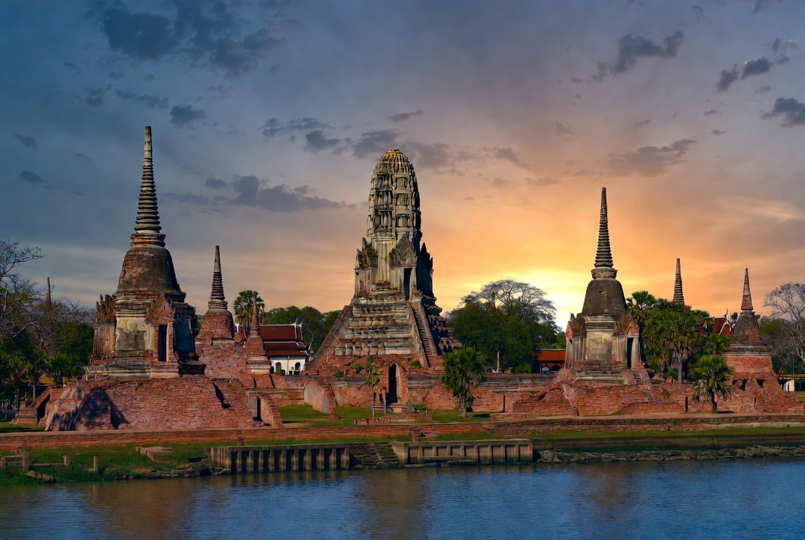 Wat Chaiwatthanaram temple complex in Ayutthaya glowing at sunset by the river
