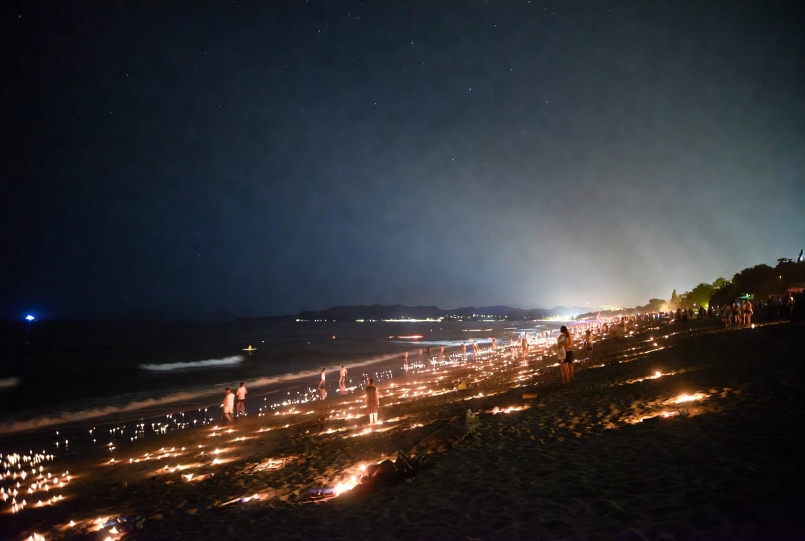 Beach at night with lights and people during a Full Moon Party on Koh Phangan