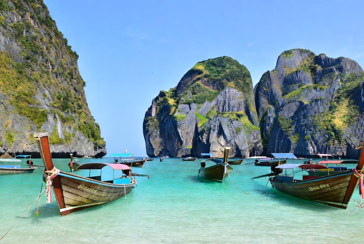 Longtail boats in turquoise water surrounded by limestone cliffs on Koh Phi Phi