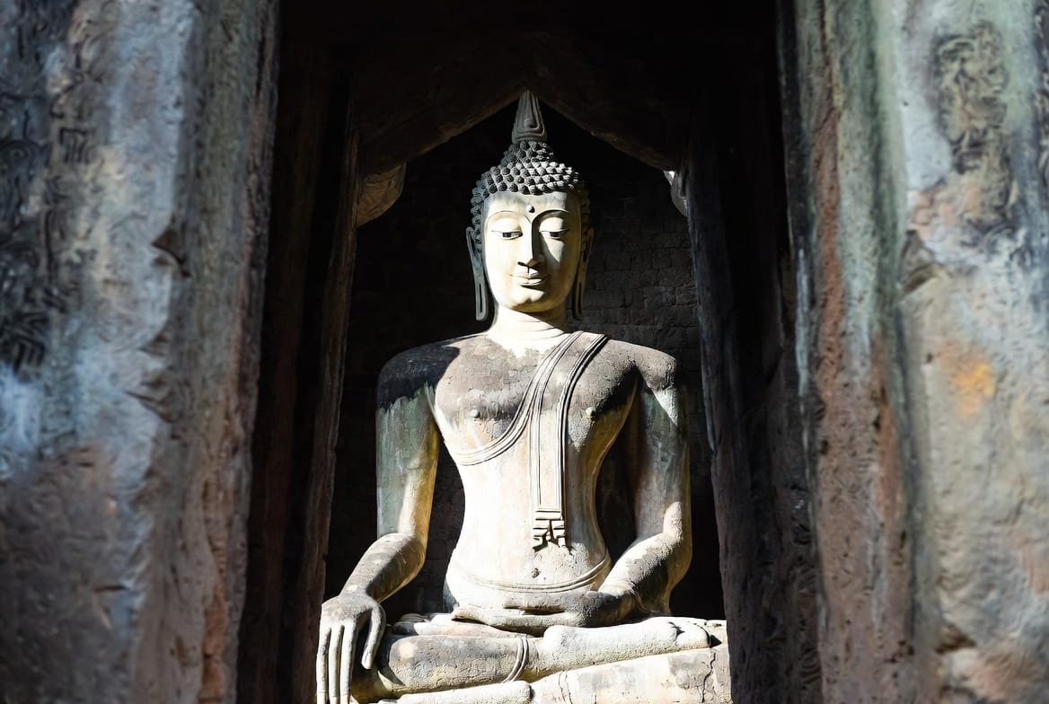 Giant seated Buddha statue at Wat Si Chum in Sukhothai framed by stone walls