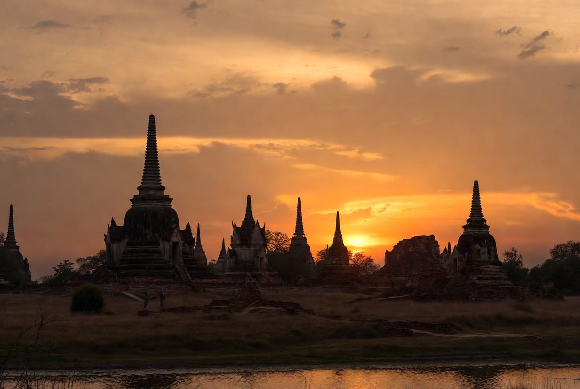 Sunset over Sukhothai temple ruins with silhouetted chedis and golden sky