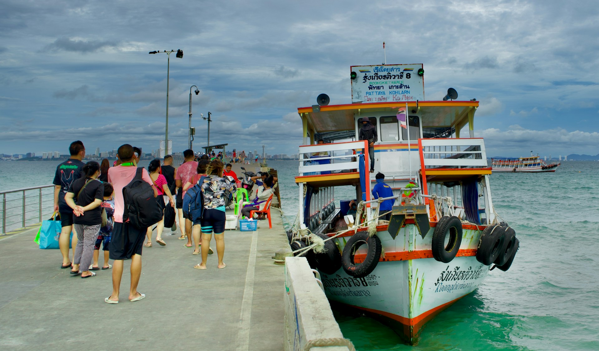 Public ferry arriving at a pier on Koh Larn with passengers and clear turquoise water
