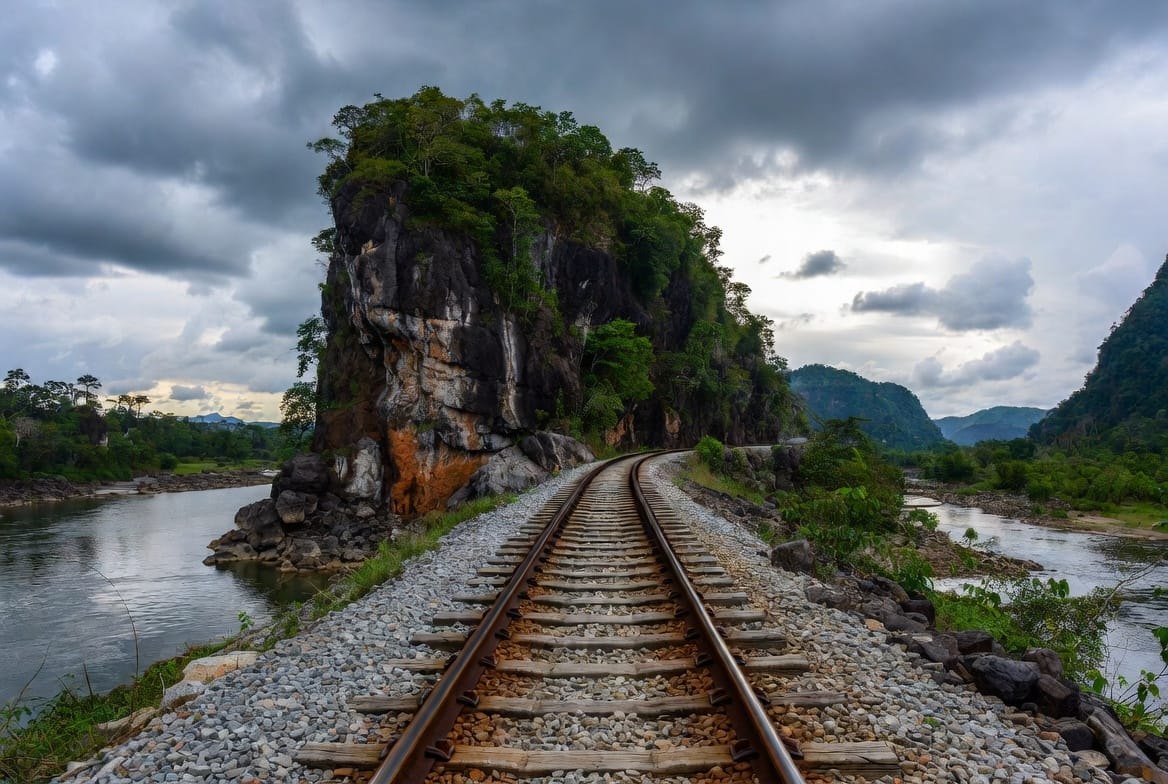 Death Railway tracks running beside a rocky outcrop and river in Kanchanaburi