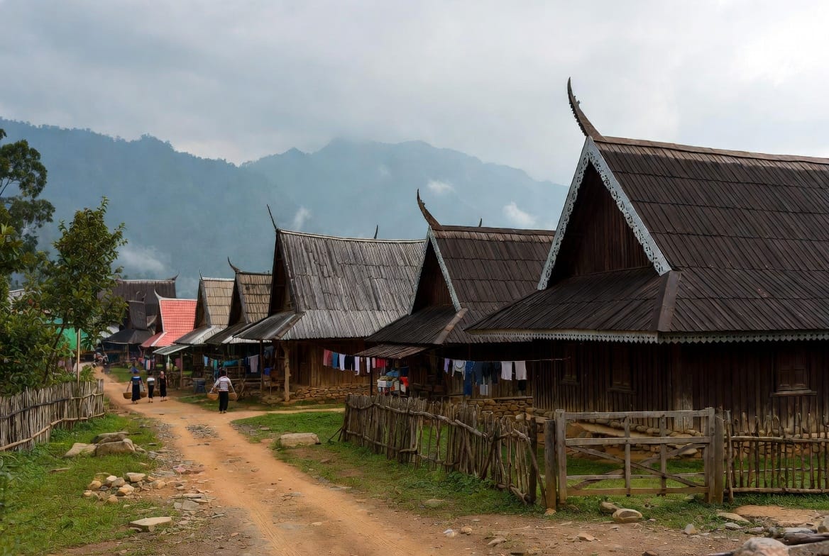 Traditional wooden houses on a quiet street in Mae Hong Son with mountains in the background