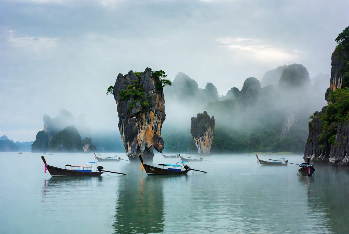 Limestone karst islands and longtail boats in misty Phang Nga Bay