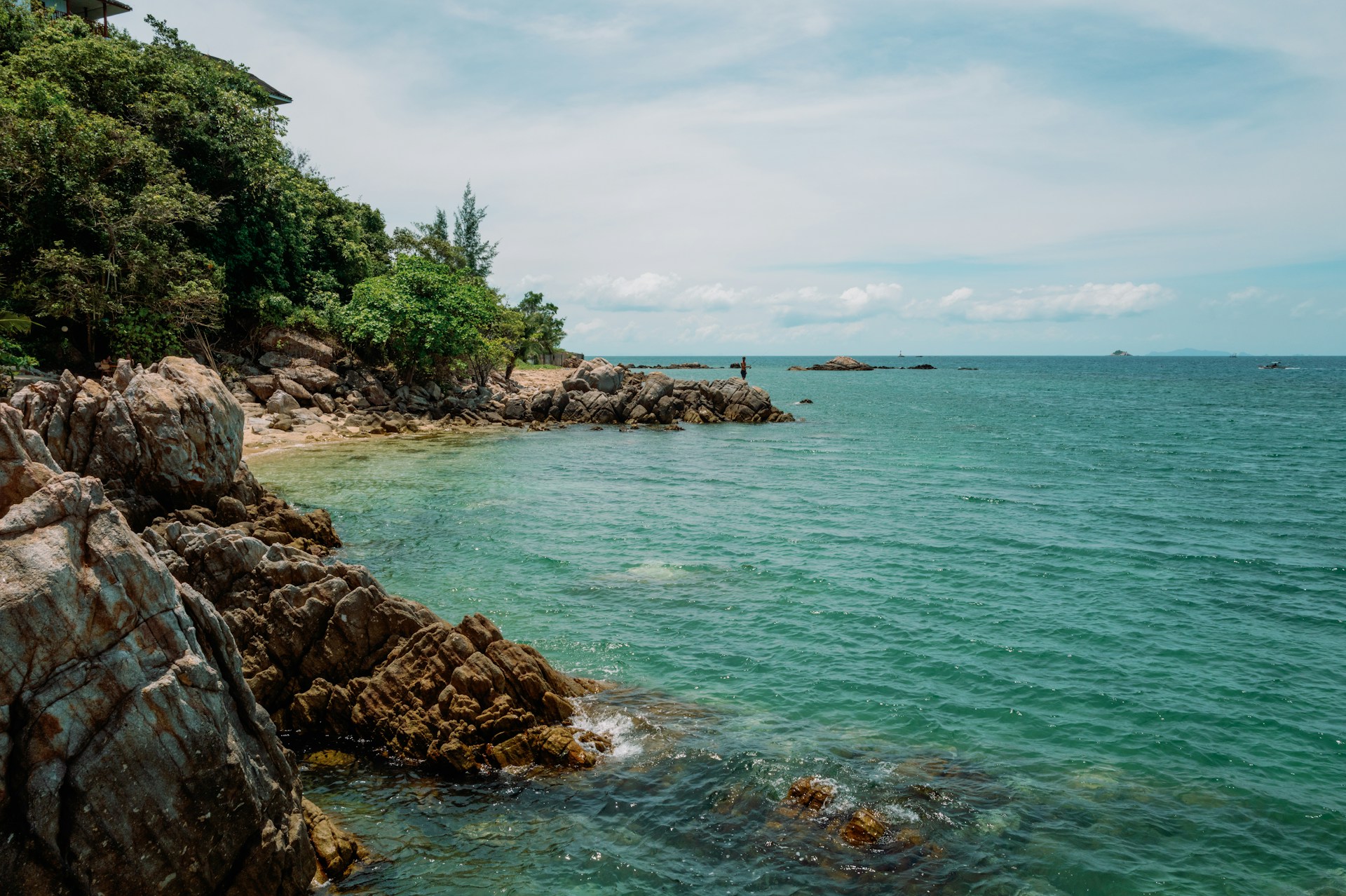 Clear turquoise water and rocky shoreline on a quieter beach of Koh Larn with people swimming