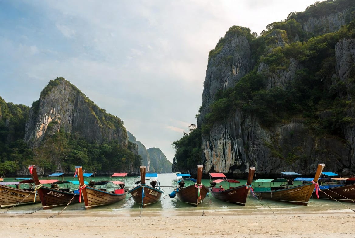 Row of longtail boats on a beach with limestone cliffs on Koh Phi Phi