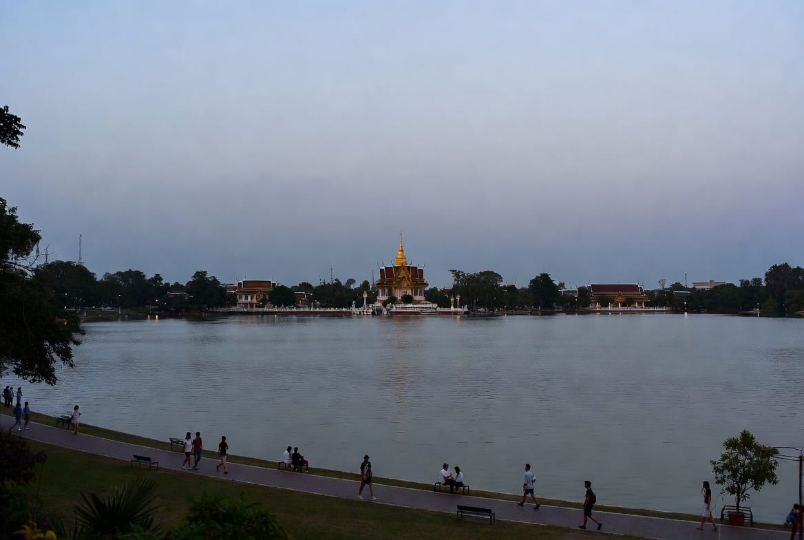 Bueng Kaen Nakhon lake in Khon Kaen with people walking and a temple across the water